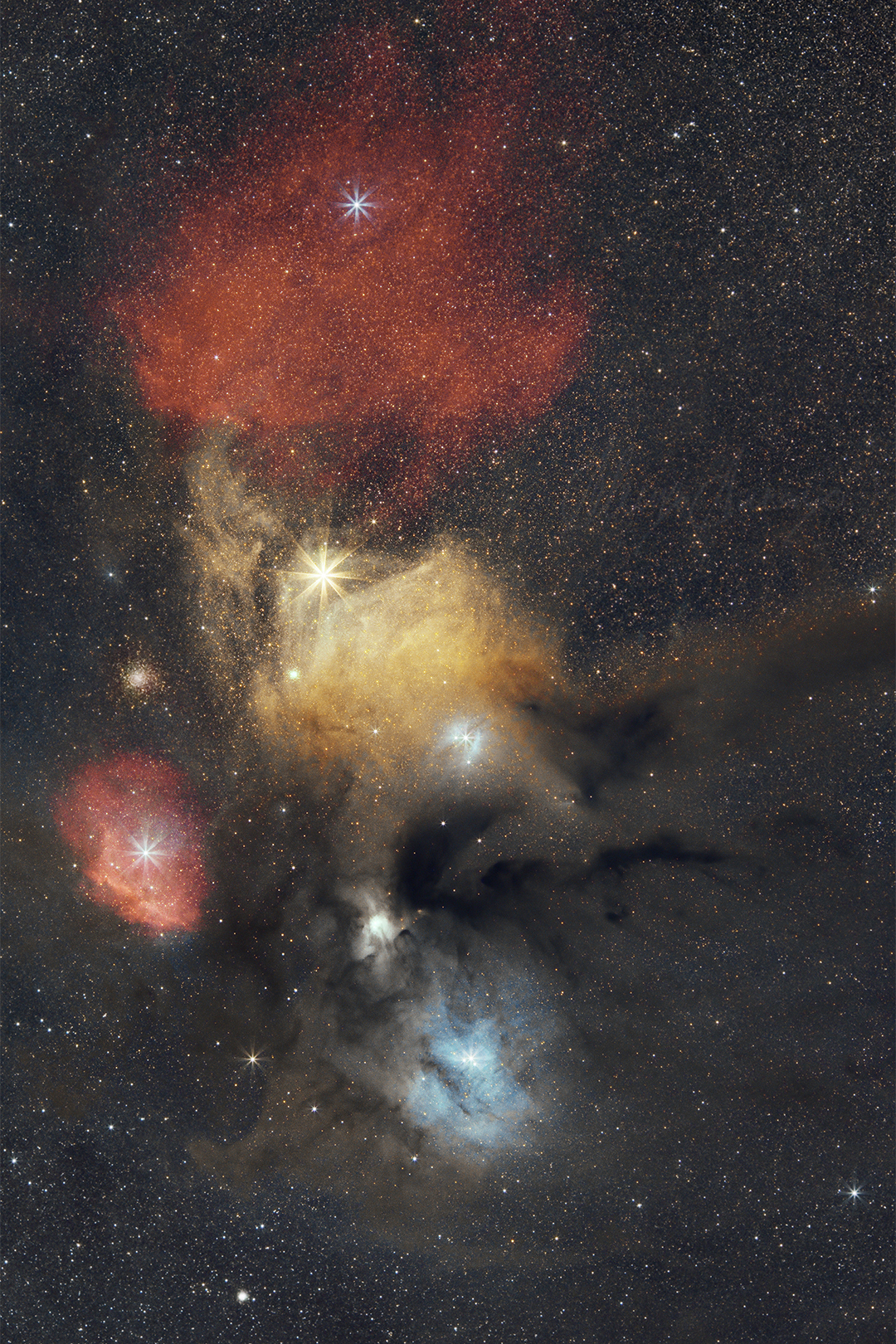 wide field image of red, yellow and blue nebulosity, biggest stars have 8-point spikes.