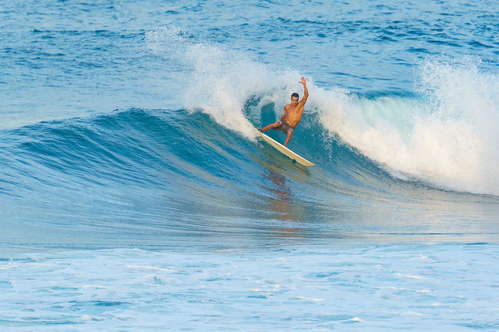person surfing with style sliding over a glassy blue wave and creating whitewater