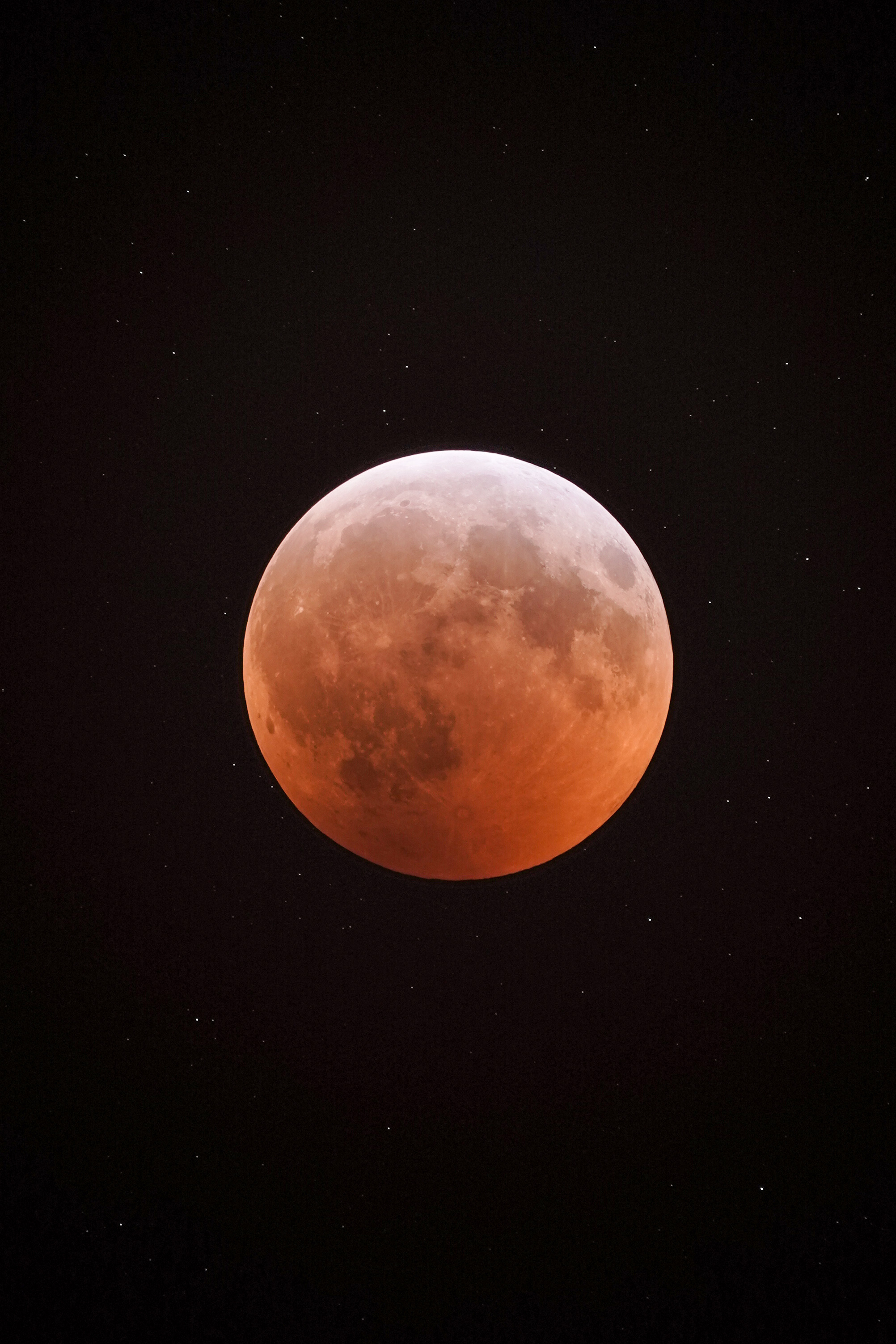 The moon during a lunar eclipse with a mix of orange and white hues against a starry background